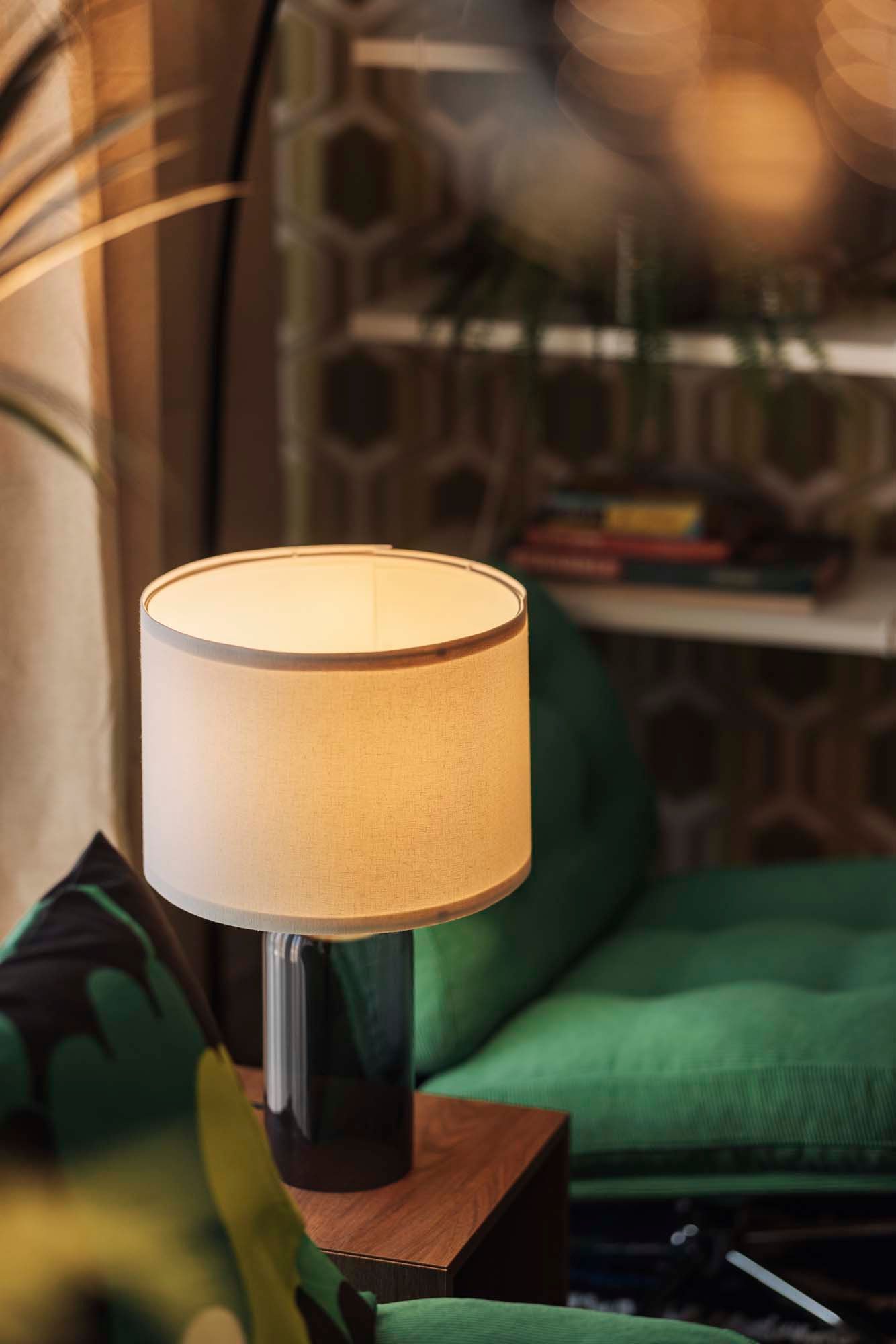A lit lamp on a side table next to a green DYVLINGE swivel armchair.