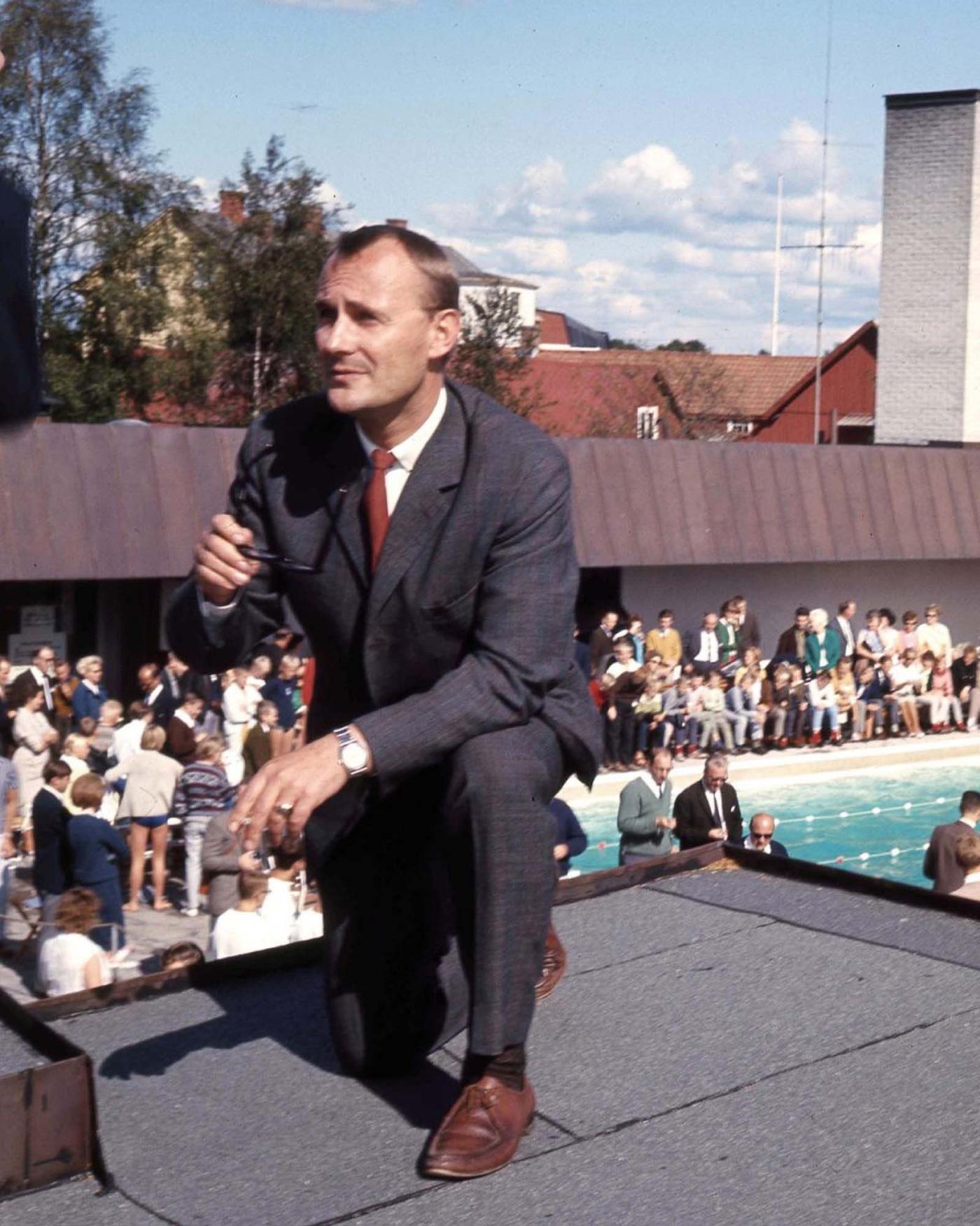 A 1964 image of Ingvar Kamprad kneeling on a roof next to the swimming pool, in front of crowds of people.