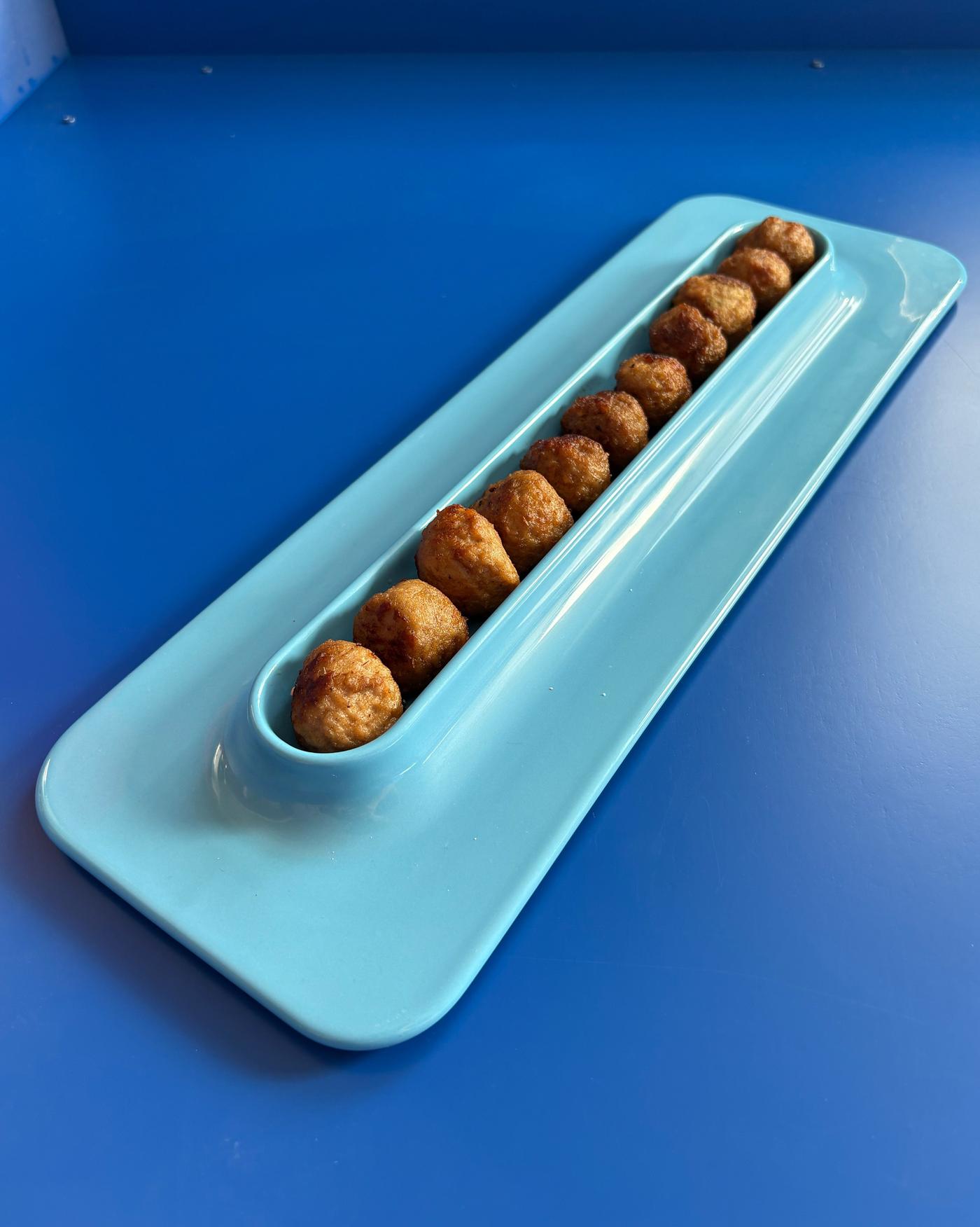 Close-up of an oblong blue plate with meatballs in a row on a blue surface.