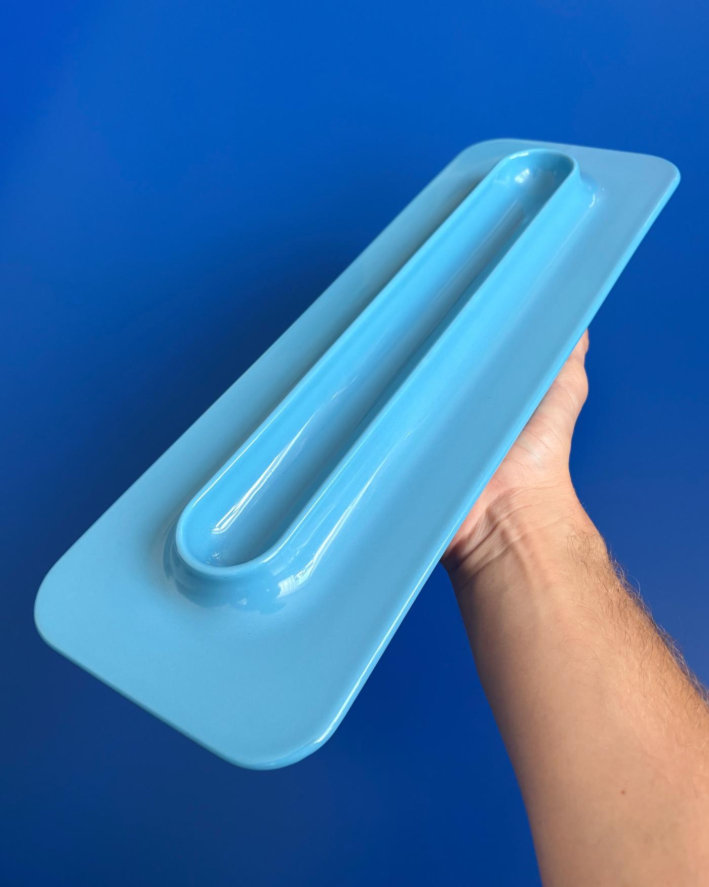 A hand holding an oblong blue plate over a blue surface, viewed from above.