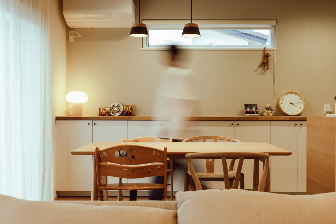 A blurred person walks past a dining table in a modern, neutral-tones living and dining area.