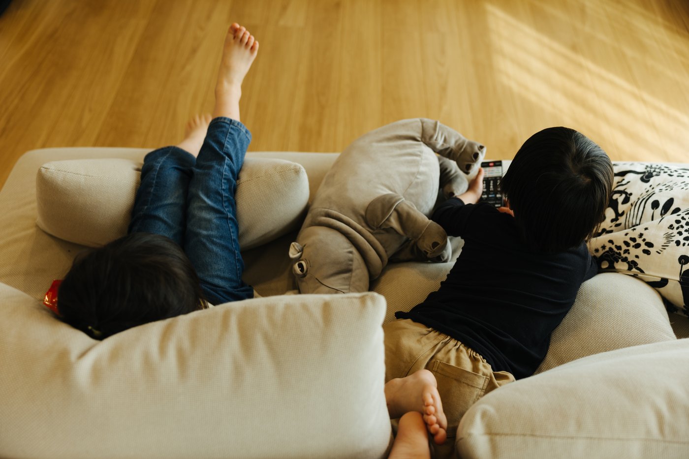 Elevated of two small children relaxing on a sofa with a hippo soft toy.