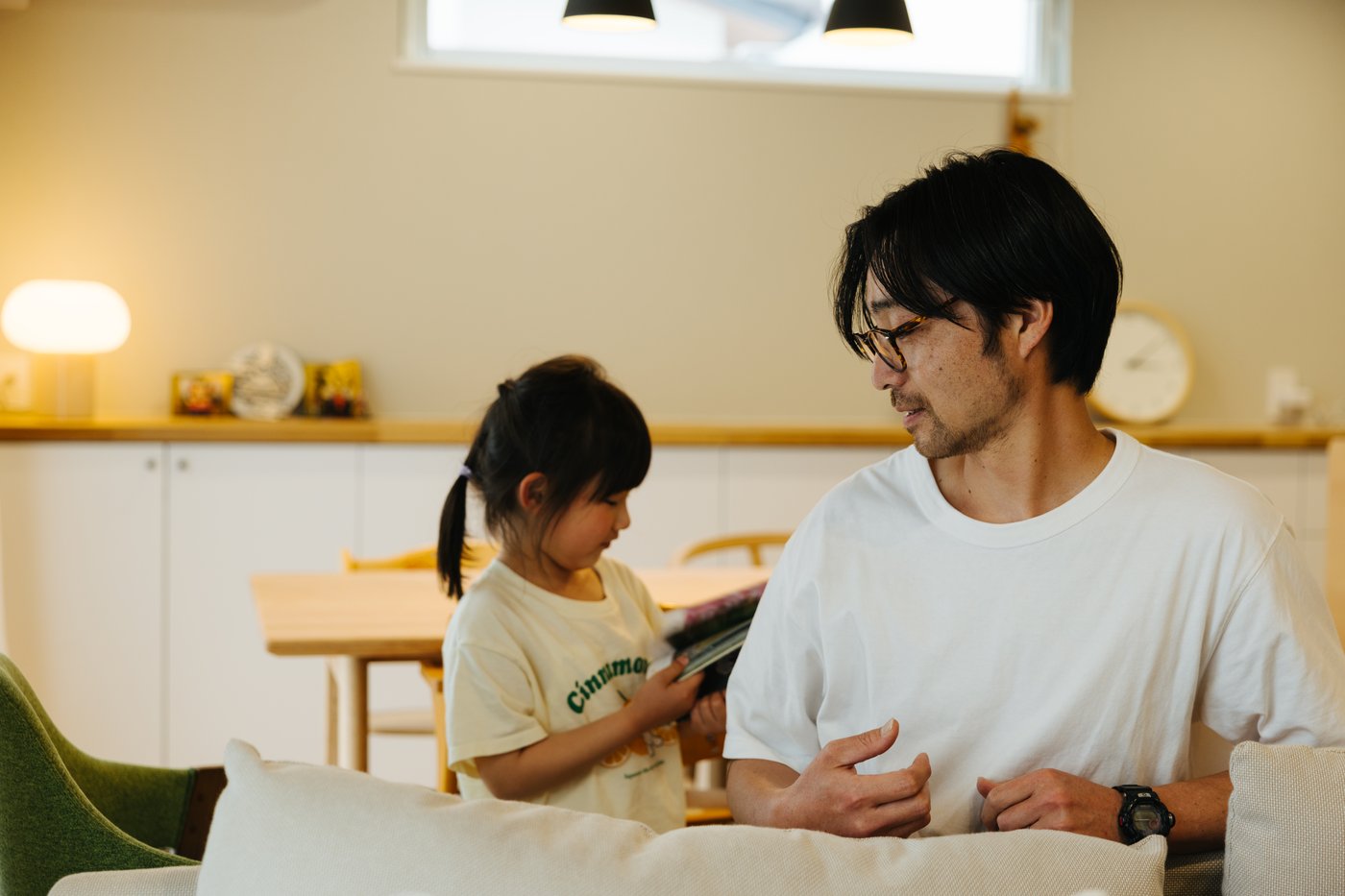 A parent and child wearing white -t-shirts interact in a white and beige open-plan dining area.
