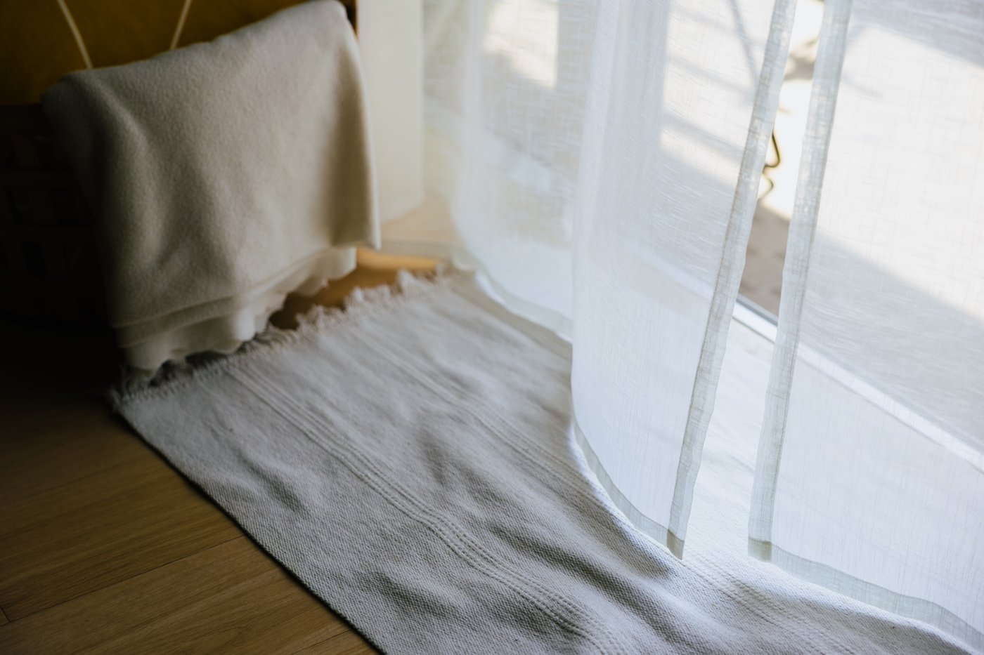Close up of sheer white curtains blowing over a white doormat by an open door. 
