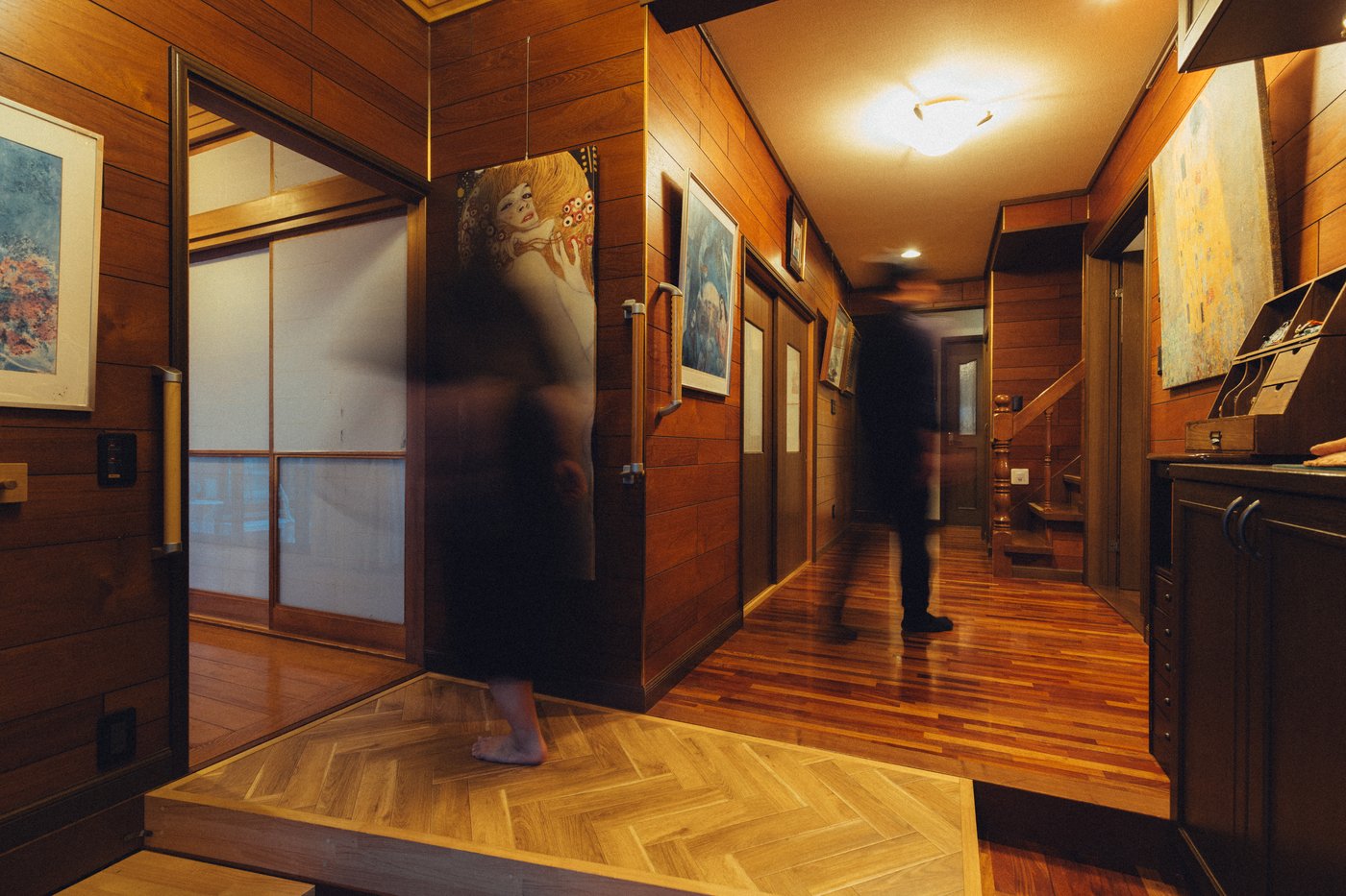 A blurred person in a hallway with wood floors and wood wall panels decorated with art.