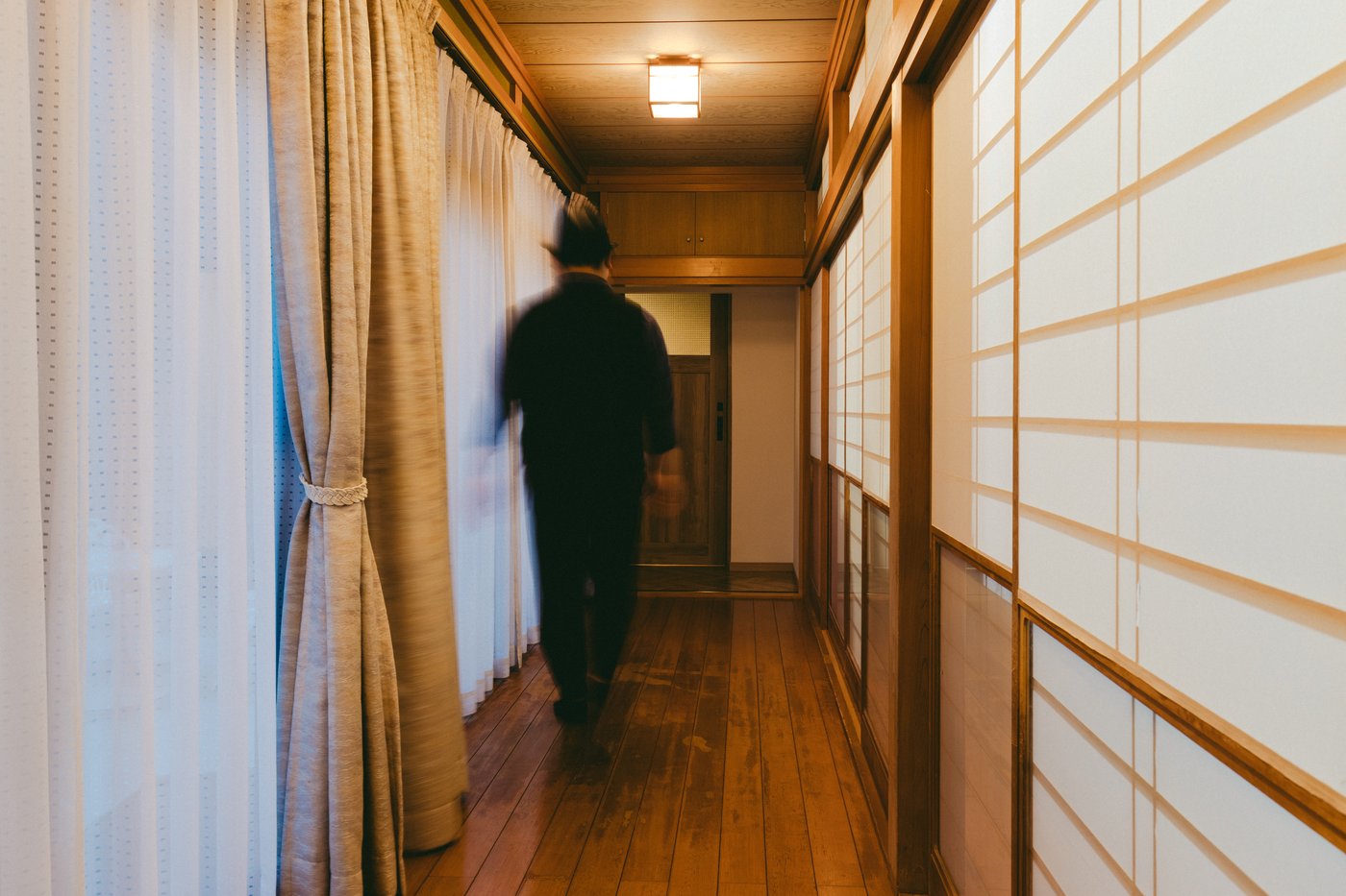 View of the back of a person walking through an illuminated hallway.