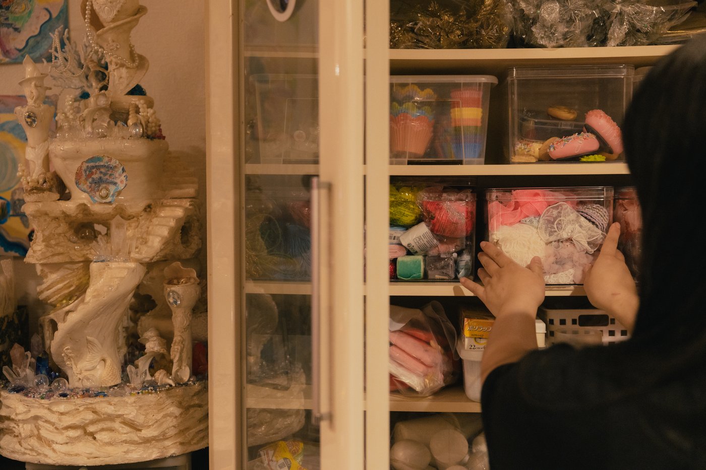 A person taking a transparent box out of a glass cabinet that is filled with craft materials. 