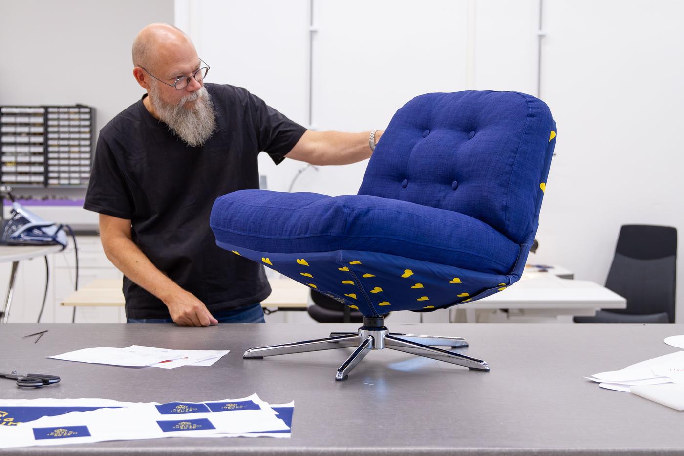 A man inspects a blue swivel chair, which stands on a work table.