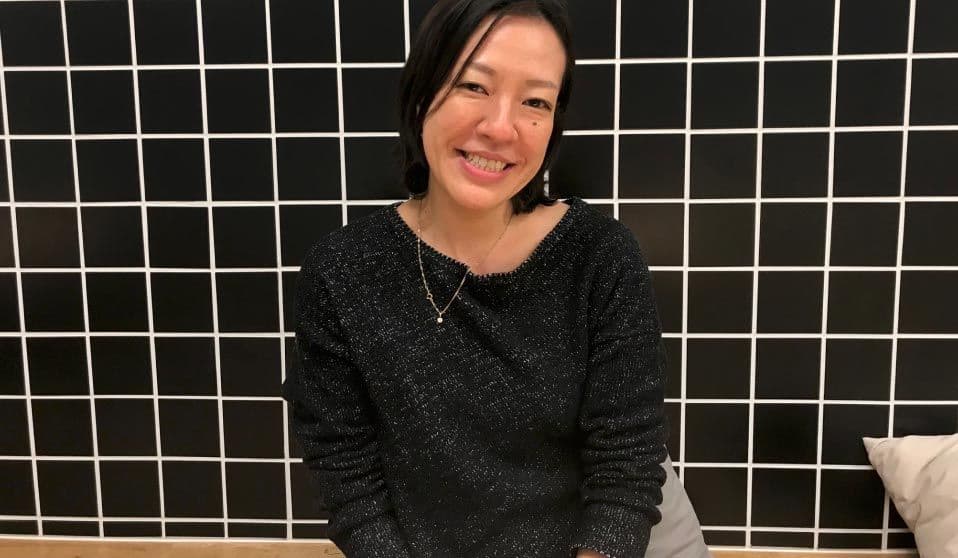 Co-worker Kimiyo sits in front of a black tiled wall