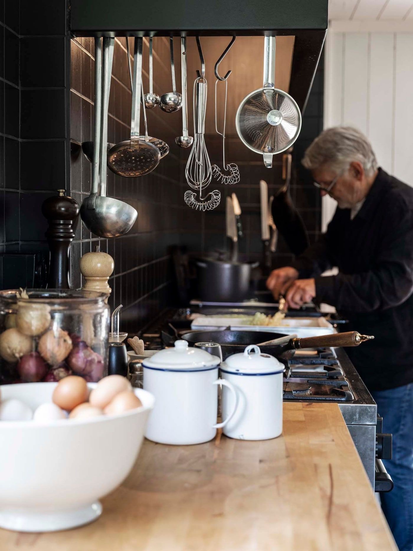 Anders cooks at the stove. Stainless steel utensils hang from hooks above the stove area.