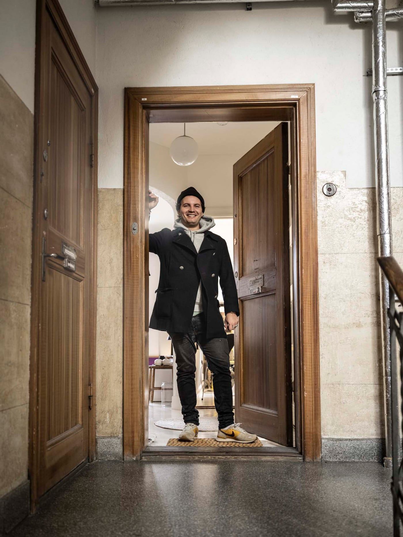 Linus stands and smiles in the doorway of his Malmö apartment.