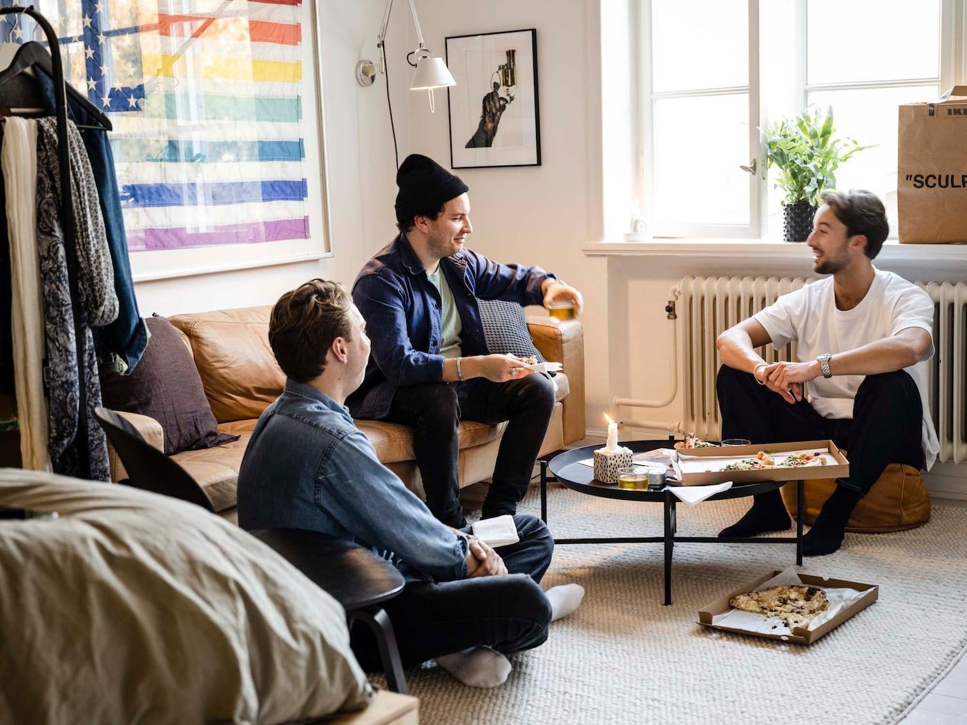 Linus and two other people sit in a living room, talking and eating pizza.
