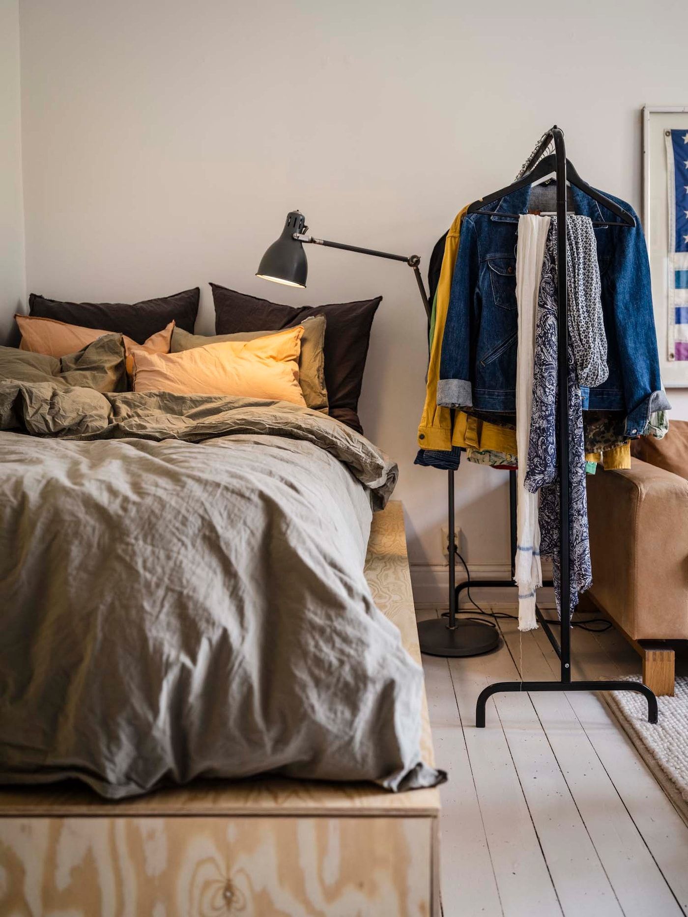 A bed on a plywood platform beside a clothes rail.