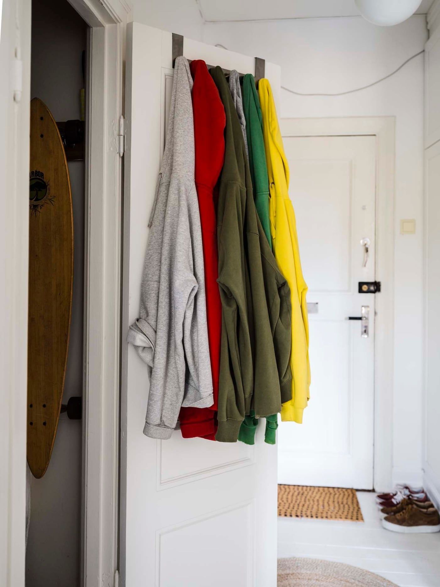 Hoodies in different colours hang from hooks behind a door.