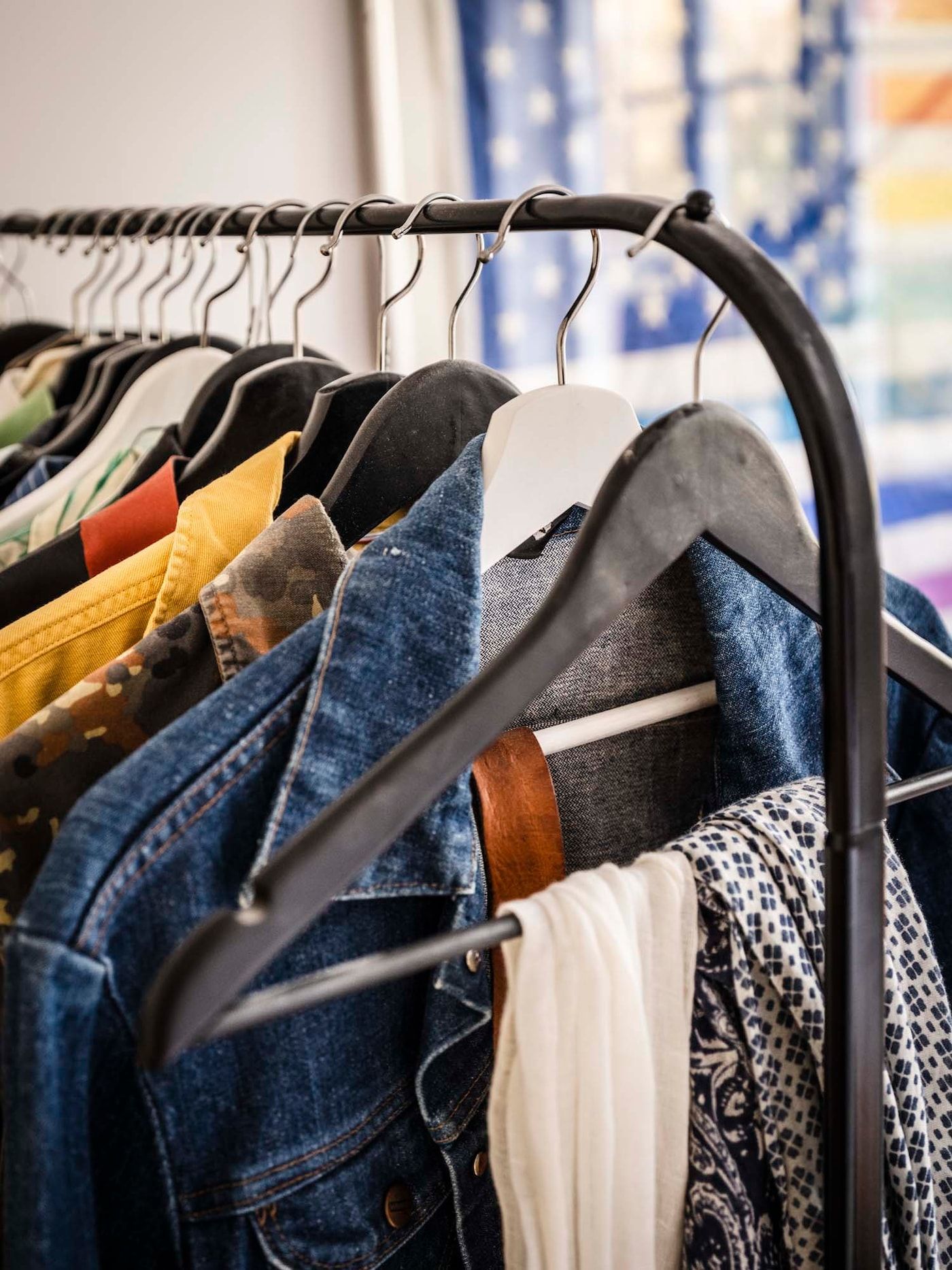 Jackets, shirts and scarves hang from a black clothes rail.