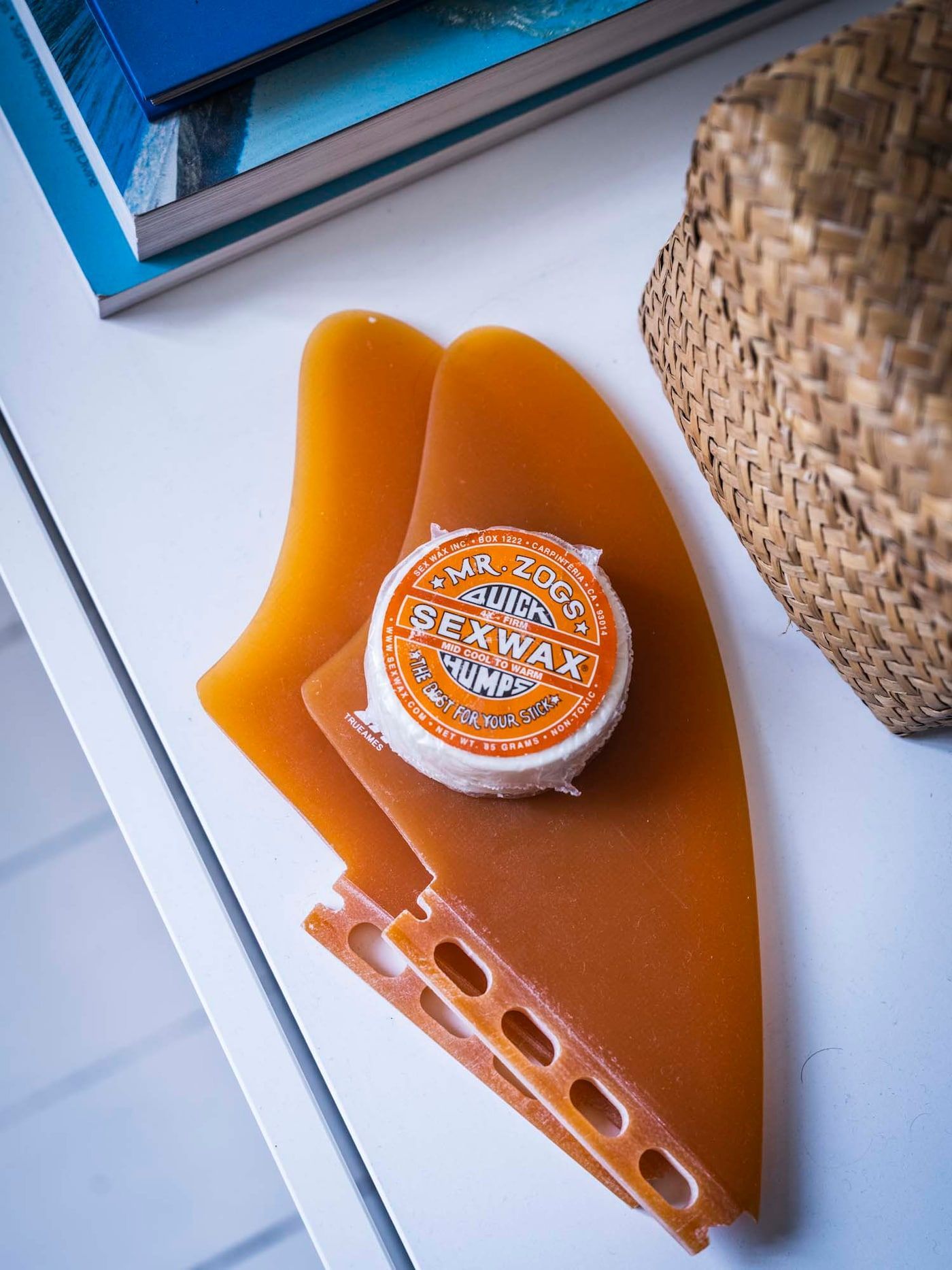 Two orange surfboard fins with a small tin of surf wax.