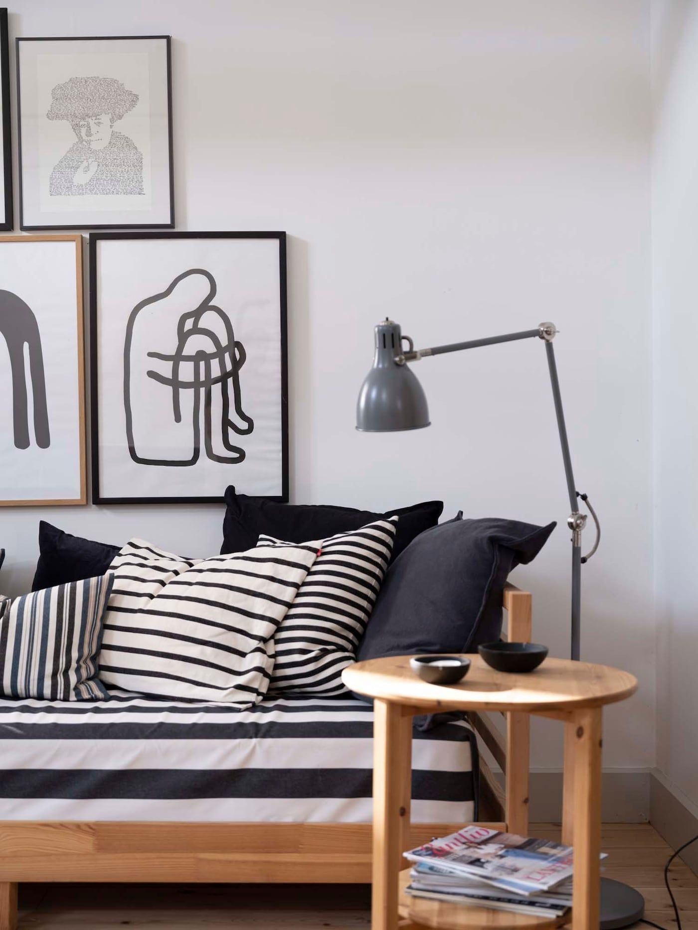A wooden day bed with a cover in cushions in graphic black and white, with contemporary artworks on the wall above.
