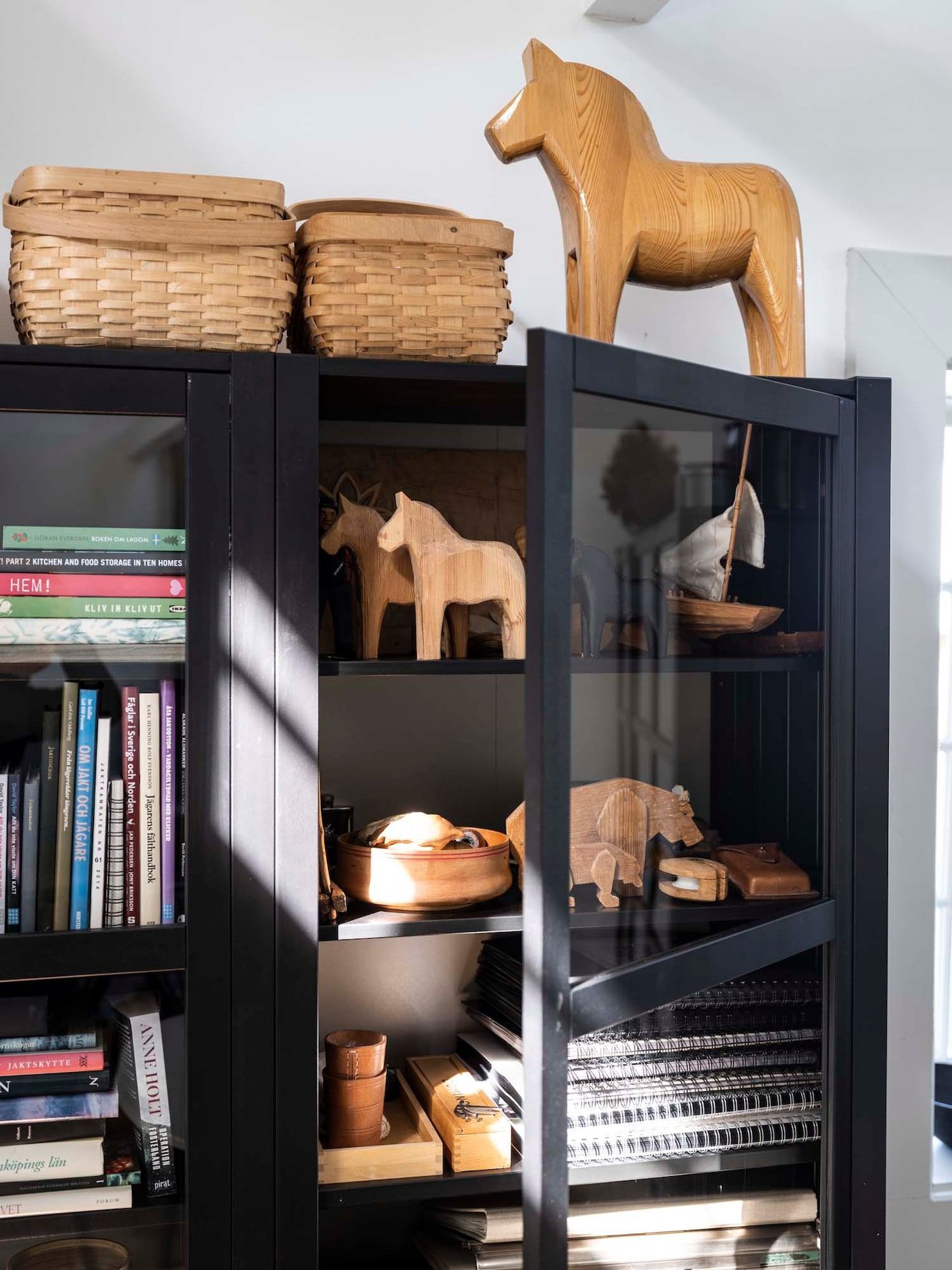 The glass-door of a black bookcase is slightly open, revealing books and hand-carved wooden objects.