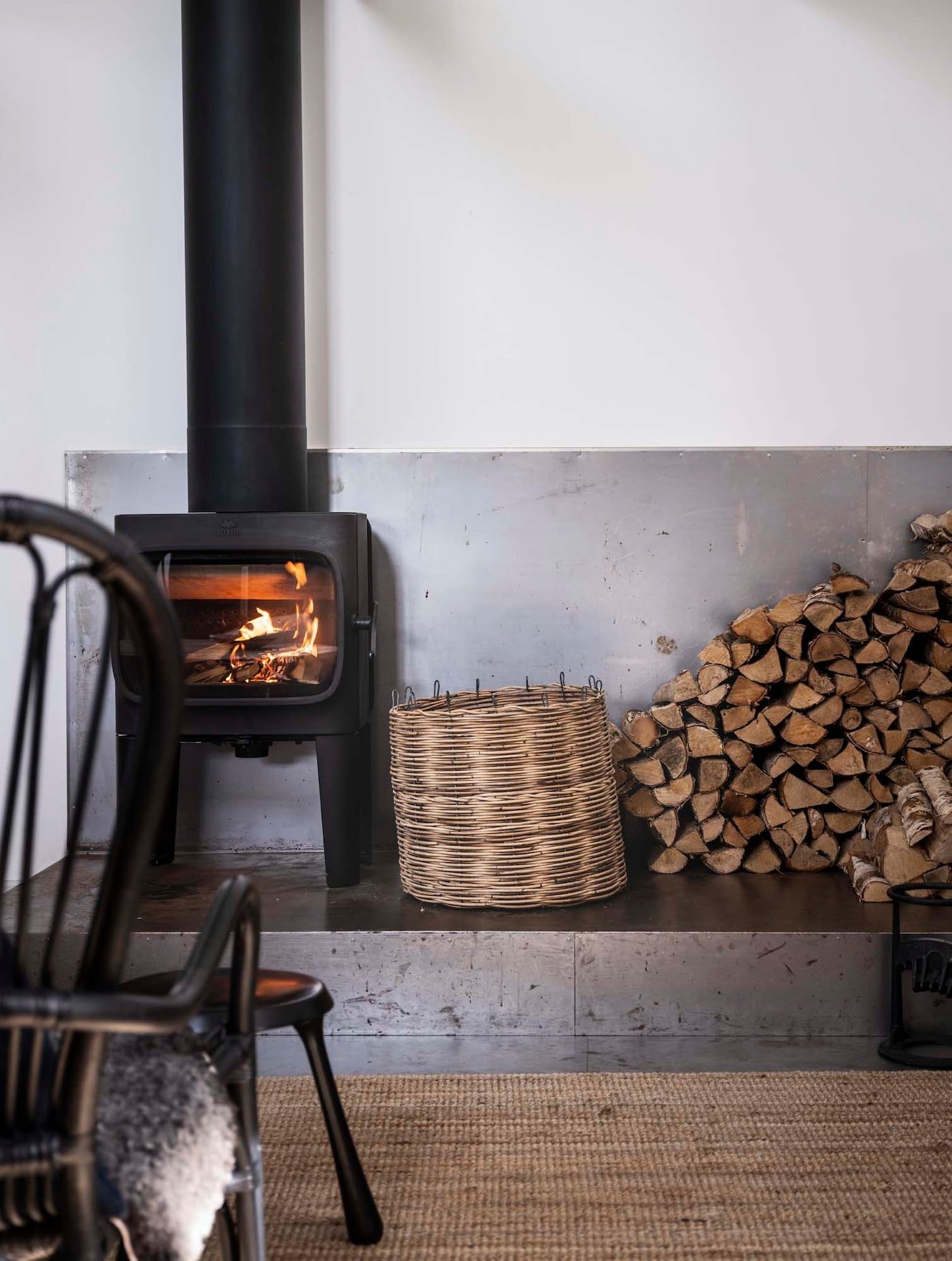 A black fireplace on a raised platform, with a pile of chopped firewood to the right.