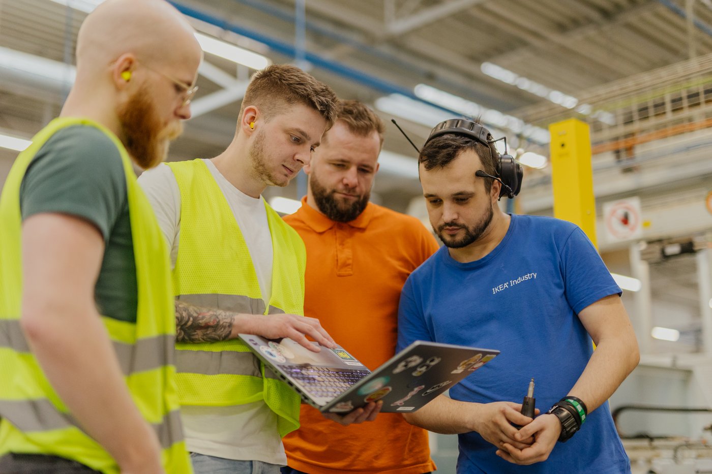 Four people looking at a laptop screen in a factory.