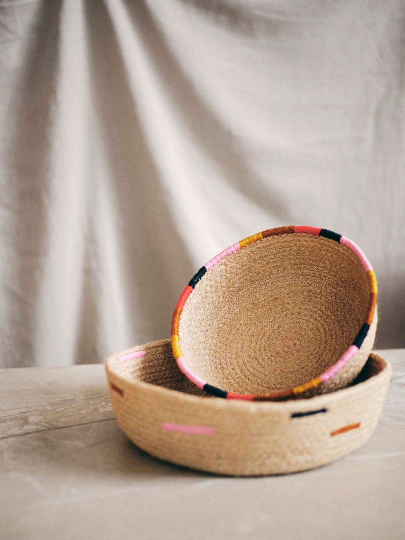 Two baskets are stacked on a table against a fabric backdrop.