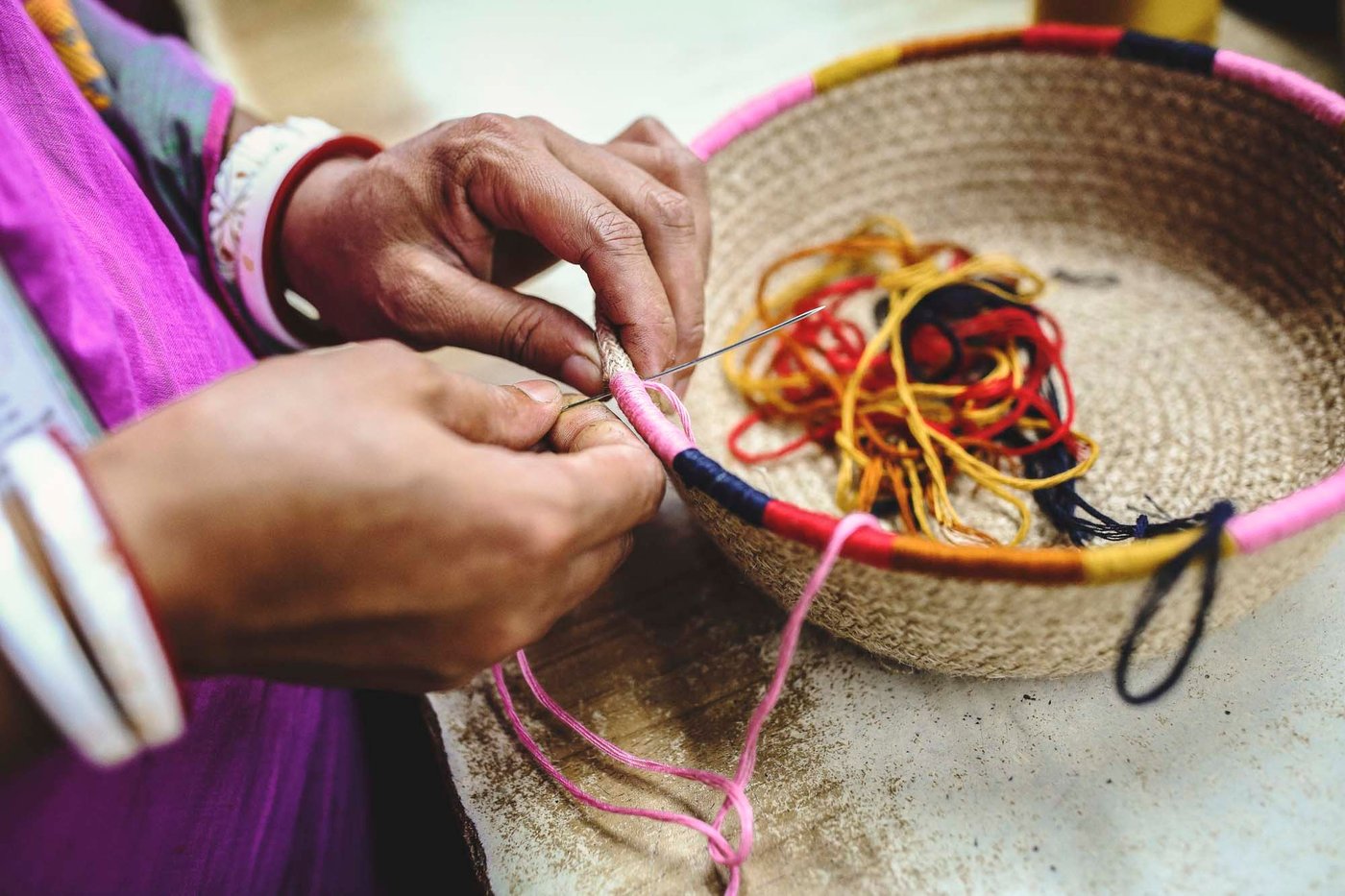 A person is sewing coloured decorative details onto a basket.