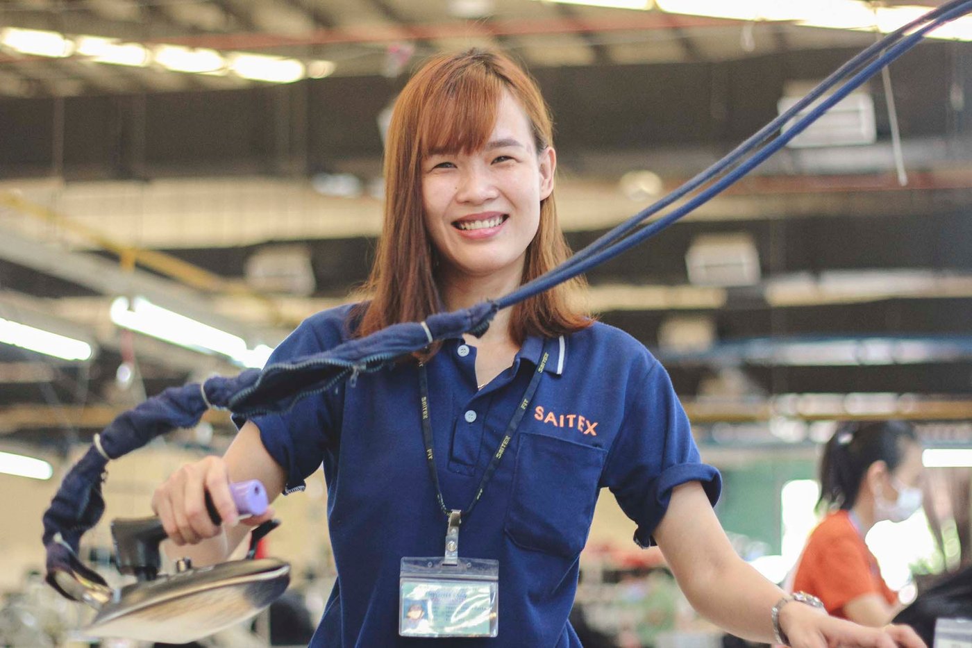 A woman smiles while holding an iron.