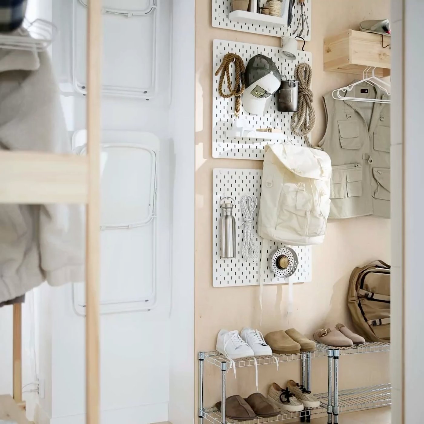 Hallway wall with outdoor gear and clothes accessories stored on white SKÅDIS pegboards, and shoes stored on two galvanised OMAR shelving units.