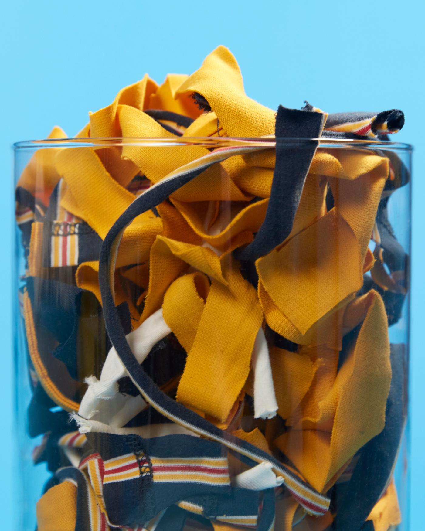 Small pieces of textiles of previous co-worker uniforms in a glass, used as a base for the VÄXELBRUK collection.