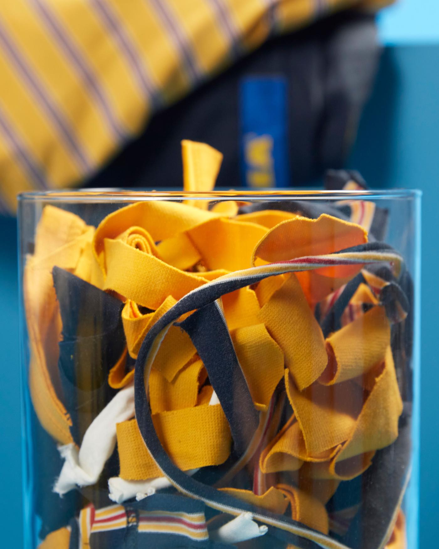 Small pieces of textiles of previous co-worker uniforms in a glass, used as a base for the VÄXELBRUK collection.