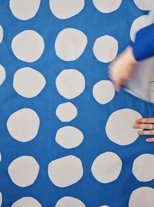 A still image showing two hands tearing a piece of blue polka dot fabric.