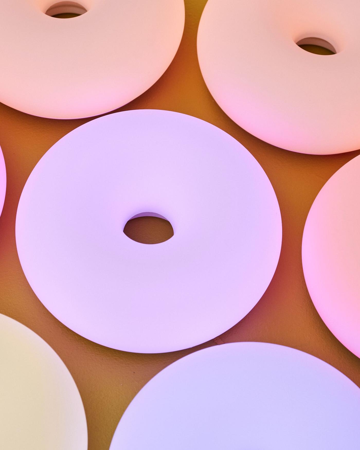 Glowing doughnut-shaped lamps in different colours against a dark yellow background.