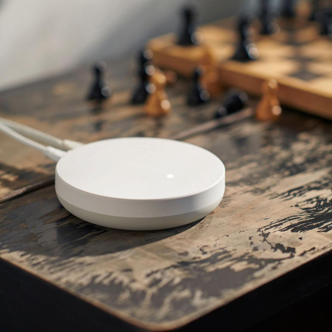 A DIRIGERA hub for smart products placed on a wooden table, next to a chessboard.