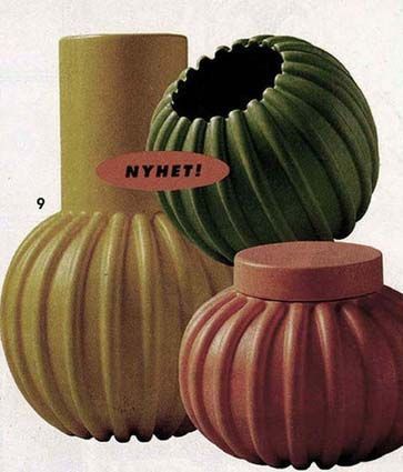 Three vases in yellow, green and orange are clustered together against a plain background.