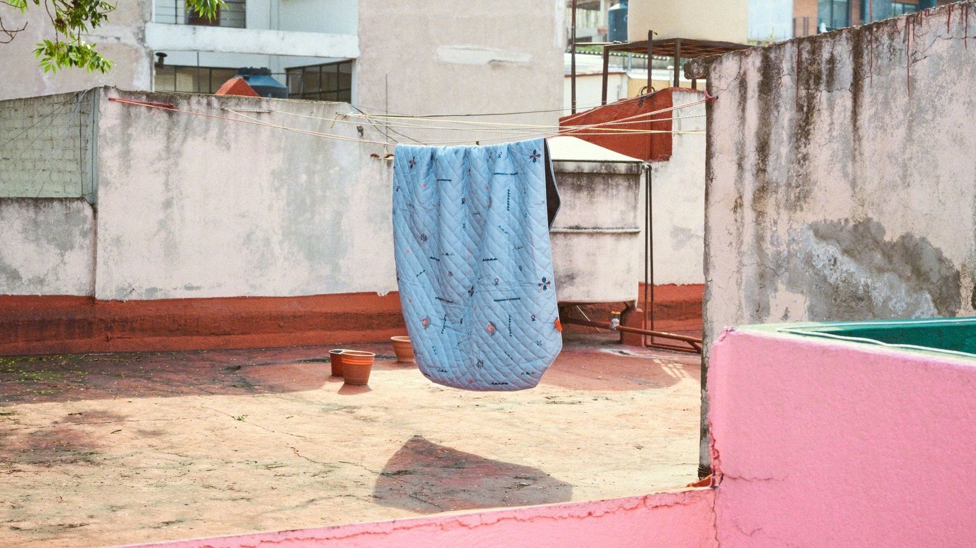 A blue ÖMSESIDIG picnic blanket hangs from a laundry line on the rooftop of an apartment block.