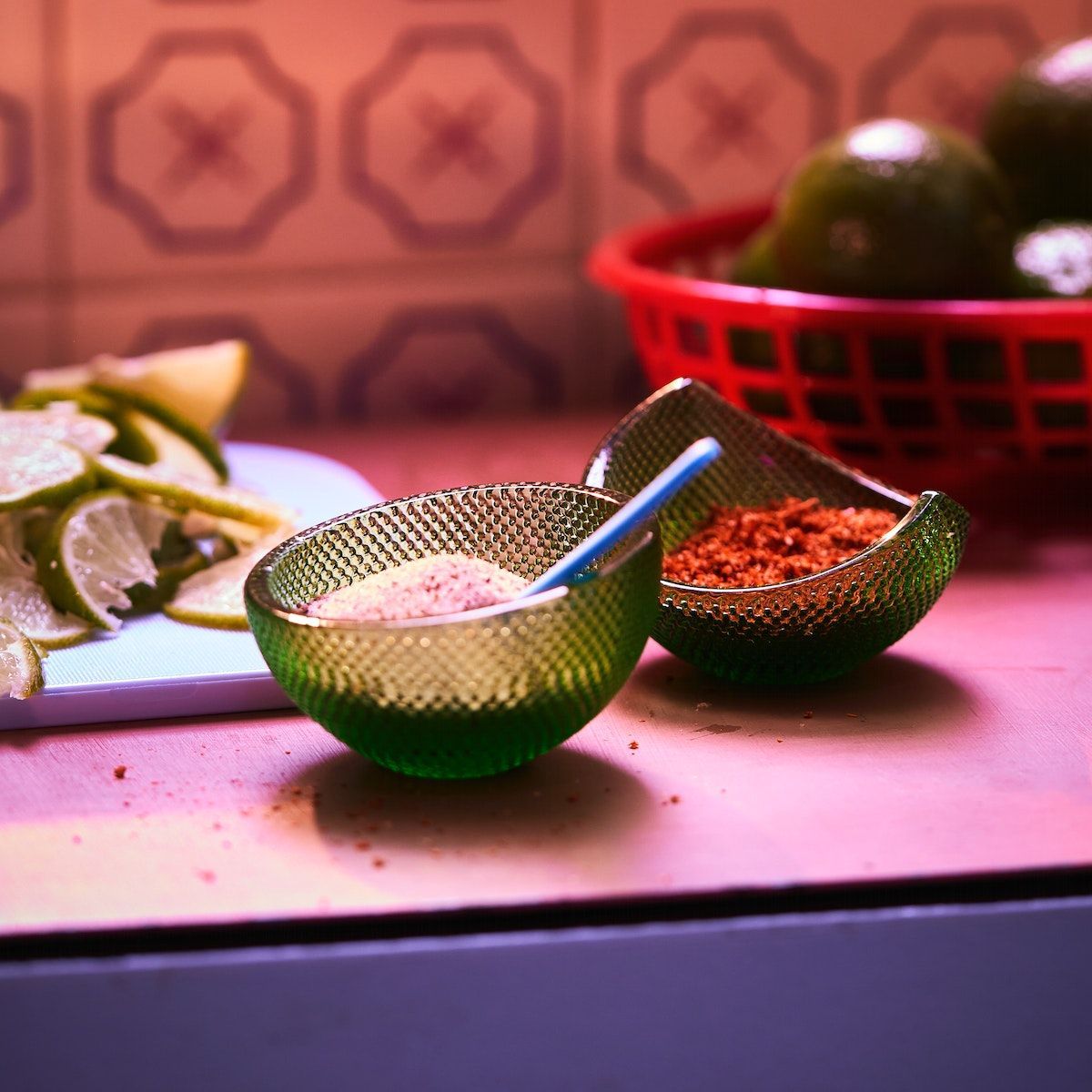 Two lime-shaped ÖMSESIDIG serving bowls filled with spices on a pink kitchen worktop.
