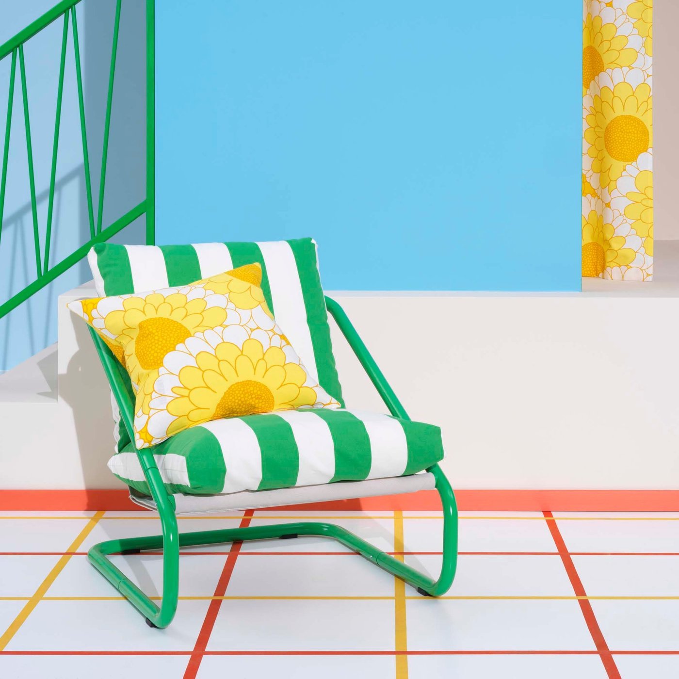 A green and white stripe ÖNNESTAD chair with a yellow sunflower print cushion sit on a white windowpane check floor, with a blue wall behind.