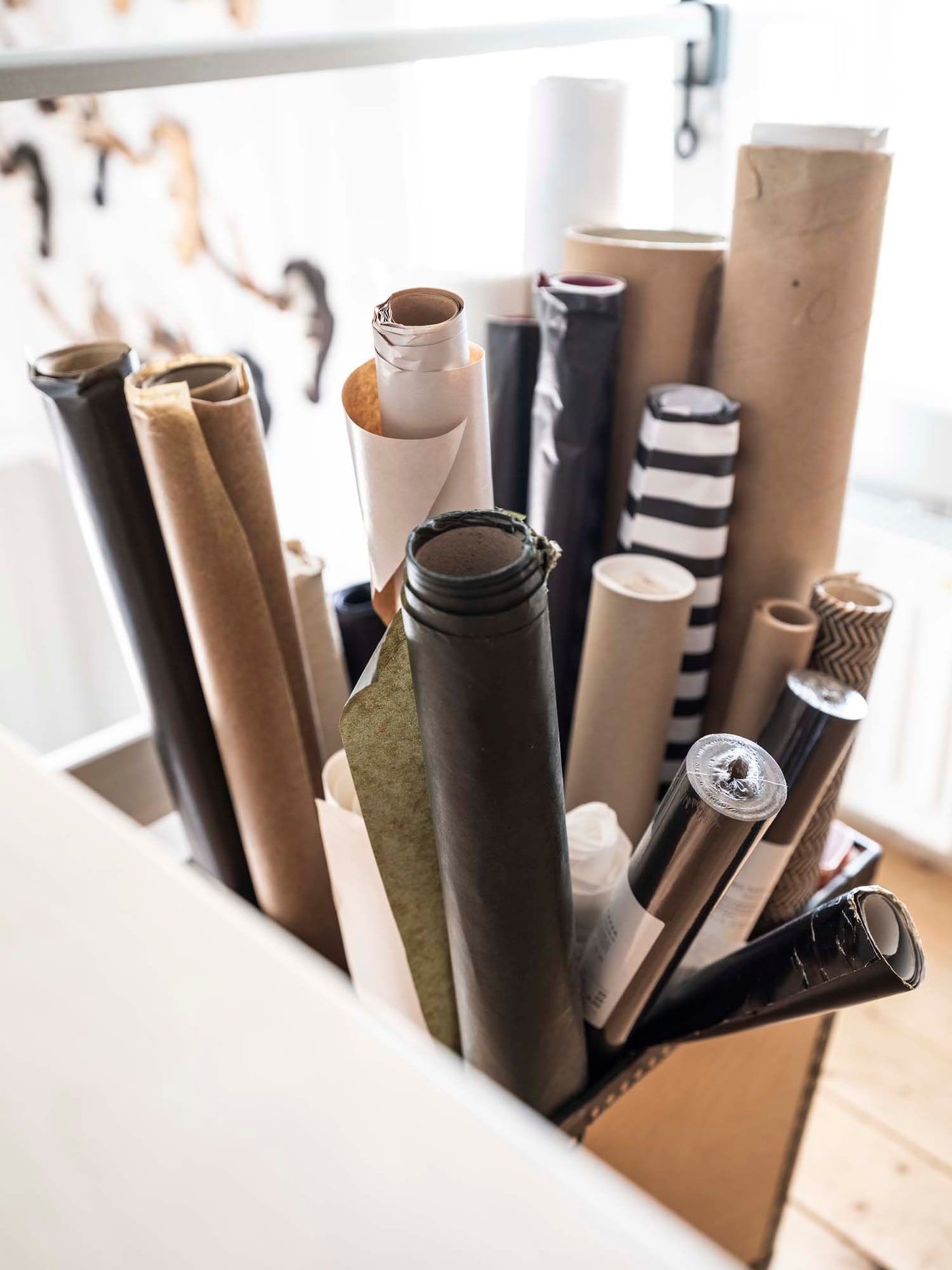 Rolls of different gift wrap in neutral colours sticking out of a storage container.
