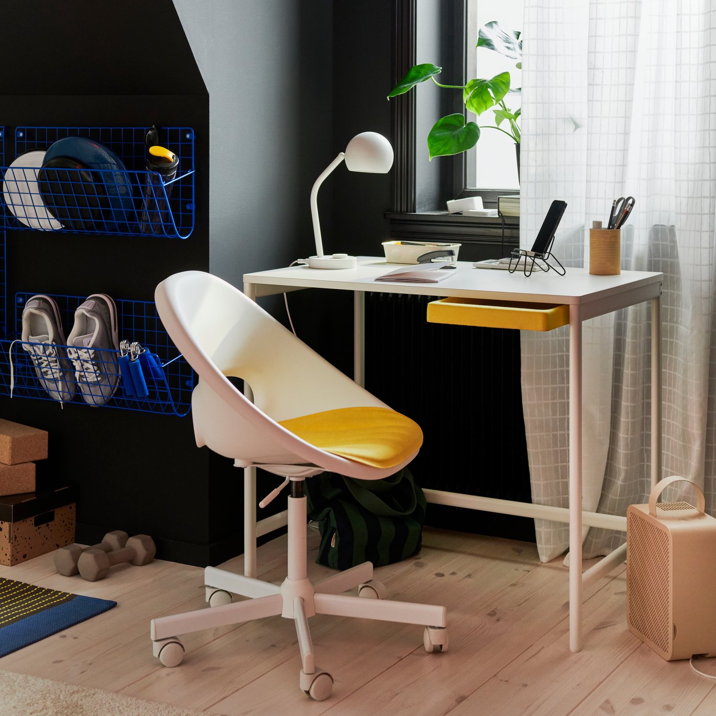 The ENKROKEN desk and LOBERGET/MALSKÄR swivel chair tucked into a corner of a bedroom with a white lamp and other desk accessories.