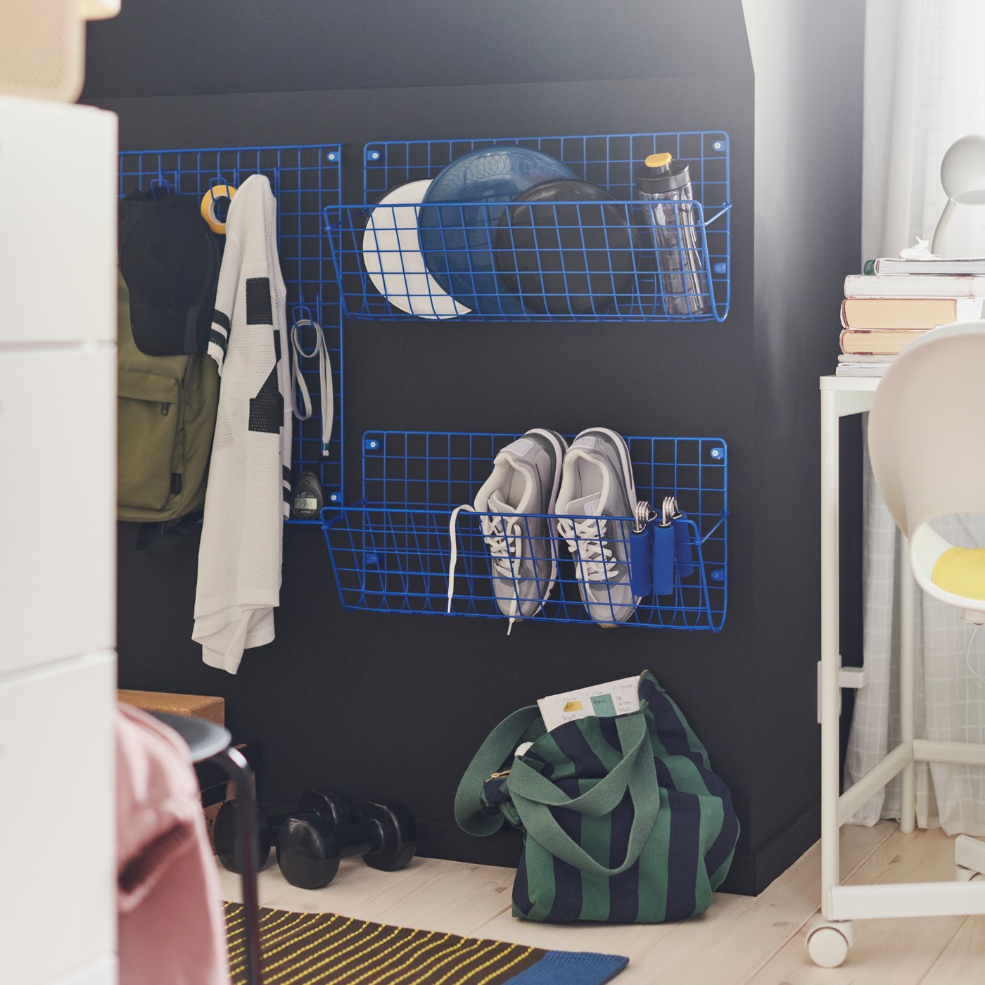 Blue GREJIG wall pockets on a black wall, holding shoes, sports gear and other accessories.
