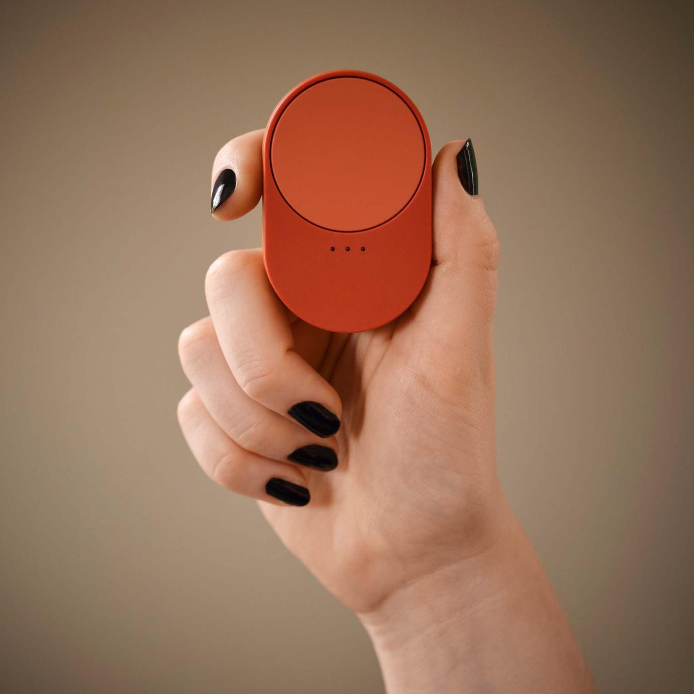 A hand with black painted nails holds a red-orange remote control.