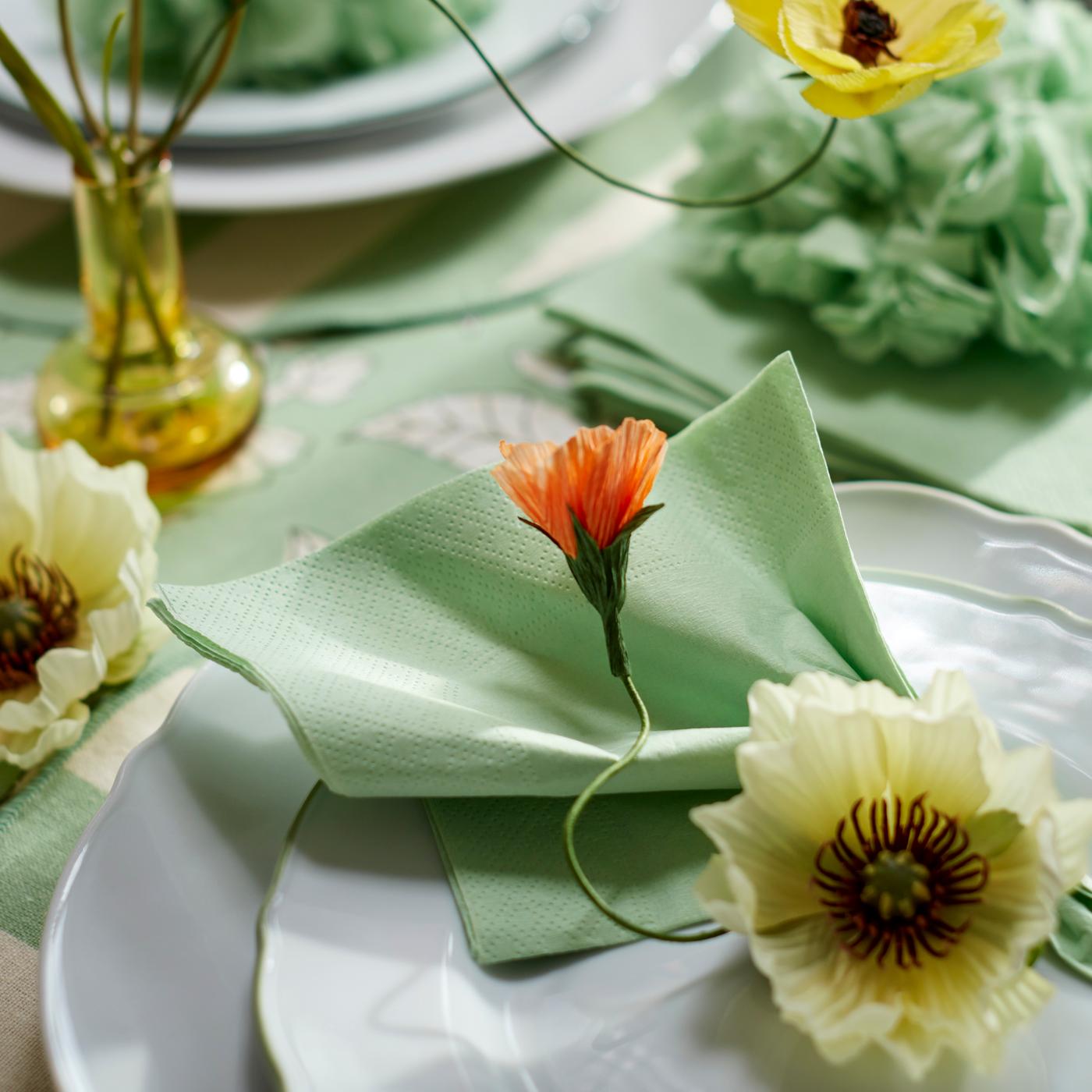 Close-up of a spring-inspired table setting with white plates and pale green napkins, decorated with GULDSPETT artificial flowers.