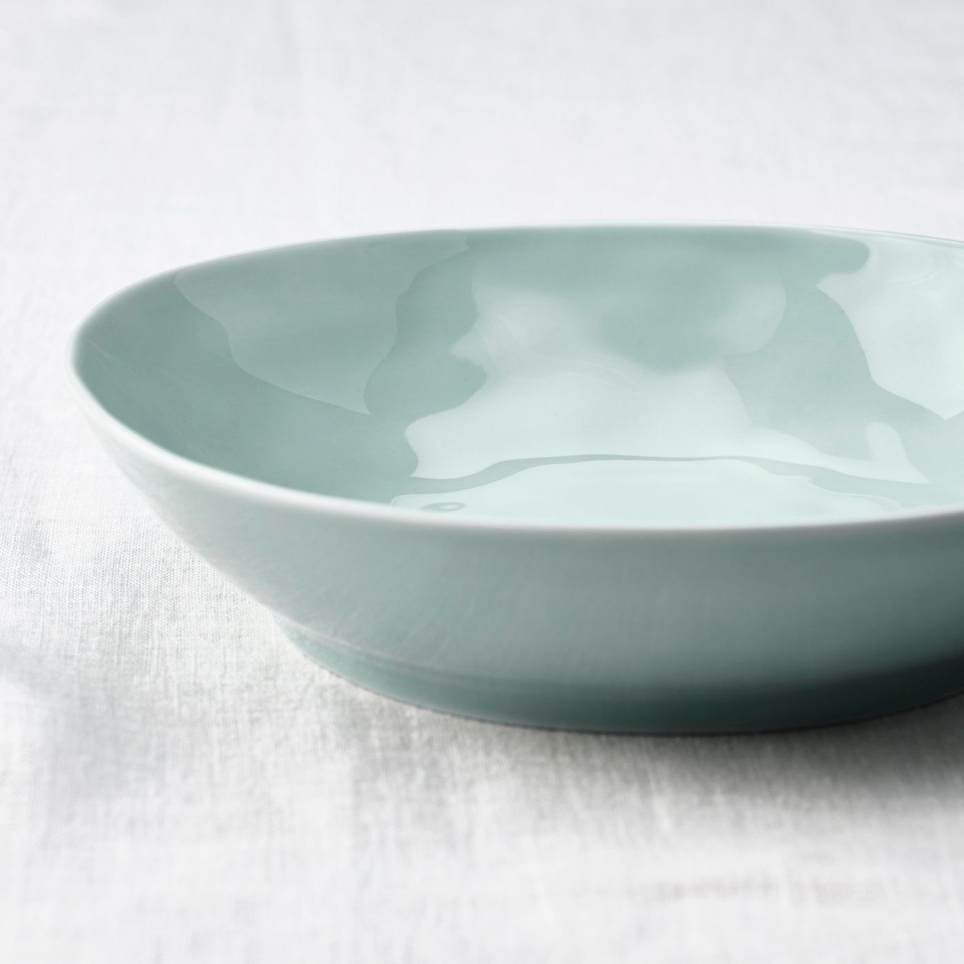 Close-up of side view of FORELLTETRA deep plate in turquoise on a white textured surface.