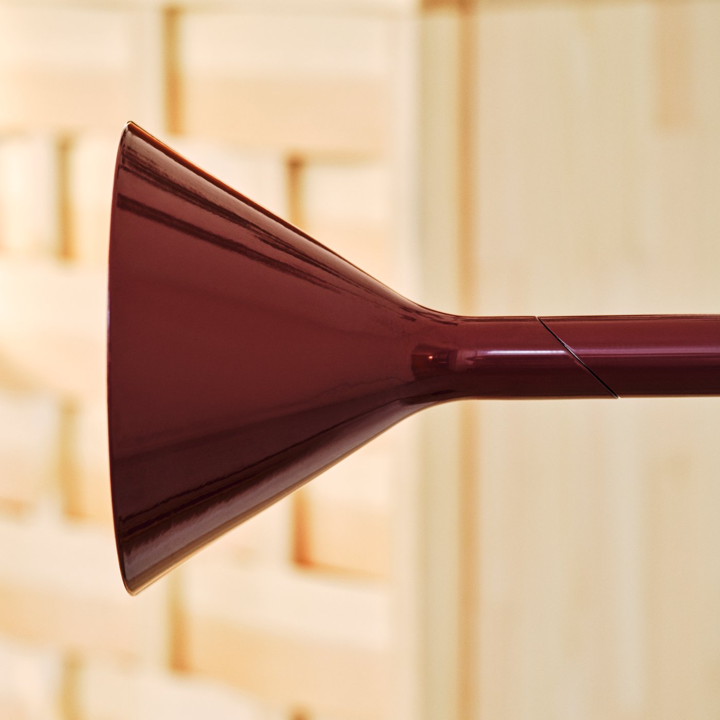 Close-up of a burgundy cone-shaped metal lamp head attached to a slim horizontal arm.