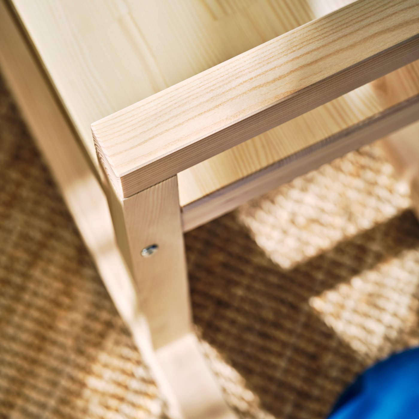 Close-up of a light wooden bench corner showing smooth edges, visible grain, and a metal screw.