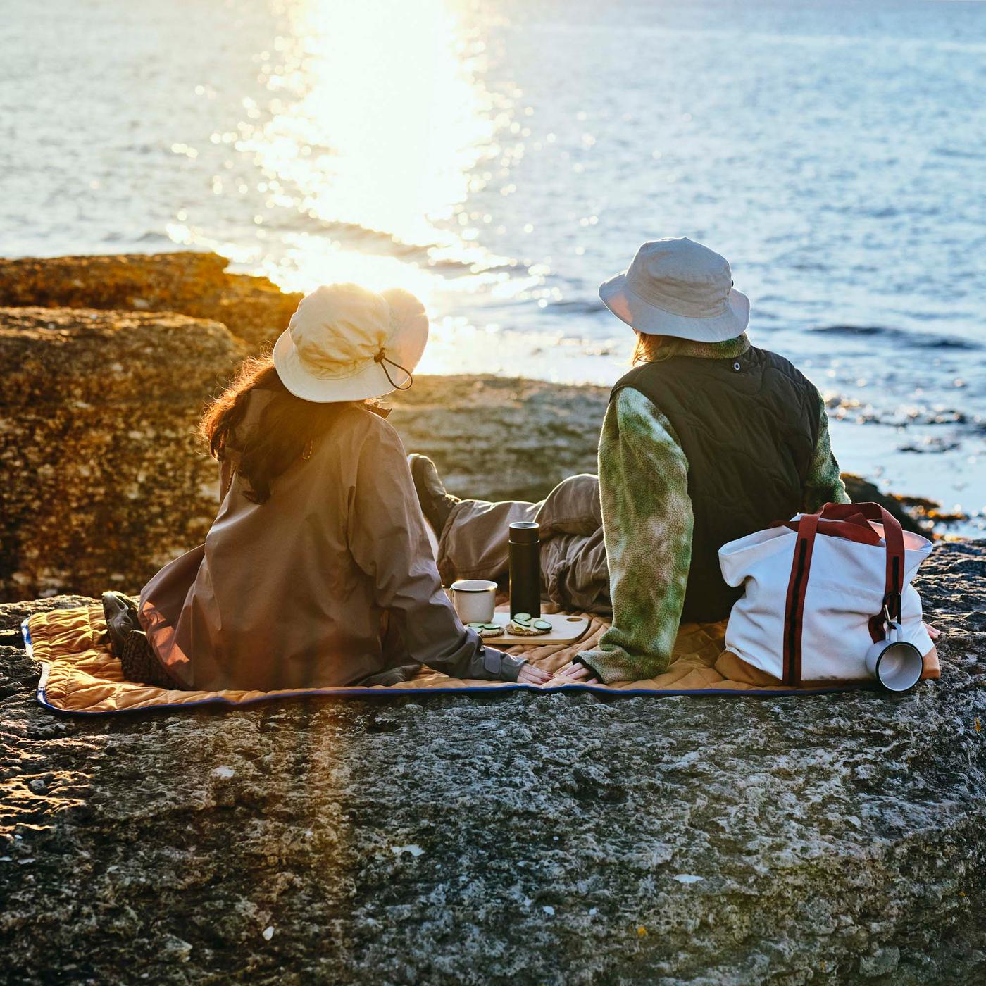 Two people sitting on a quilted orange picnic blanket looking out to sea.