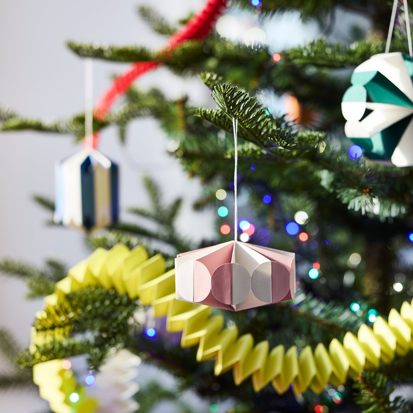 Colourful paper ornaments hanging from decorated Christmas tree branches.