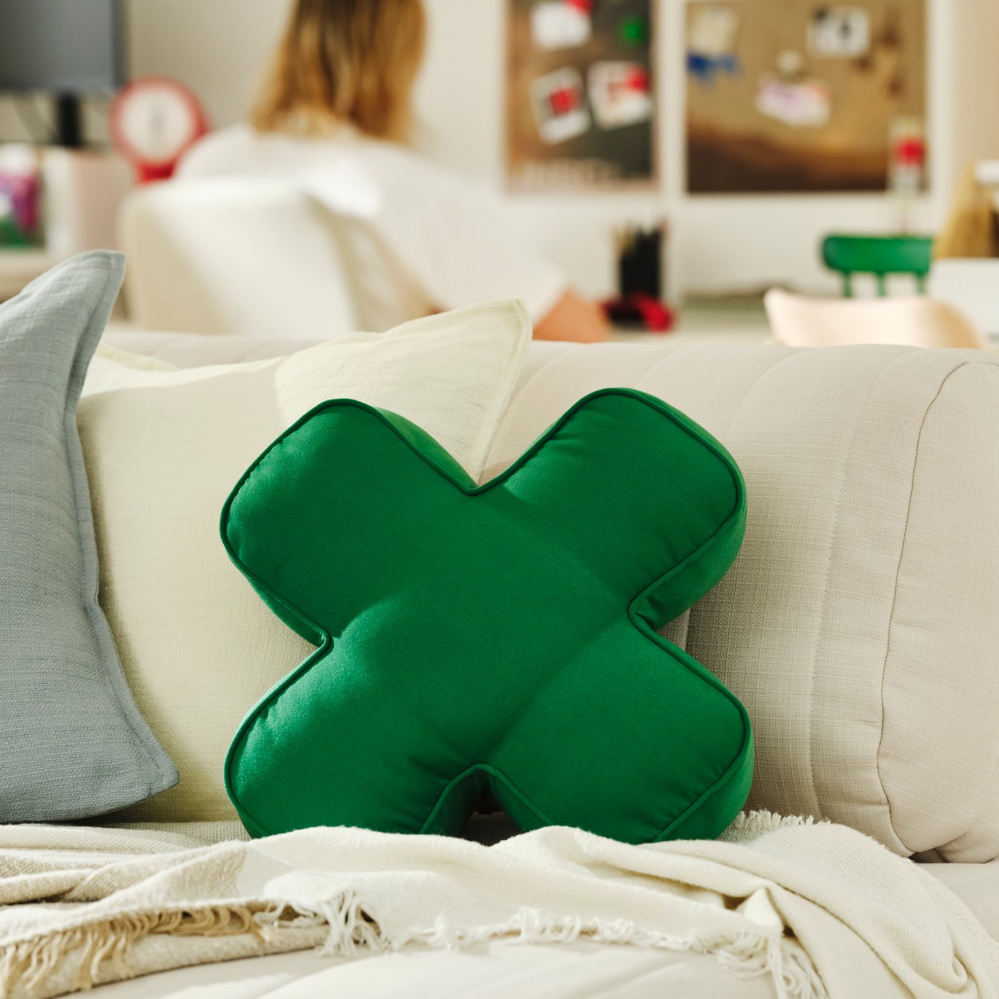 A green cushion inspired by the directional pad of an Xbox controller placed on a sofa.