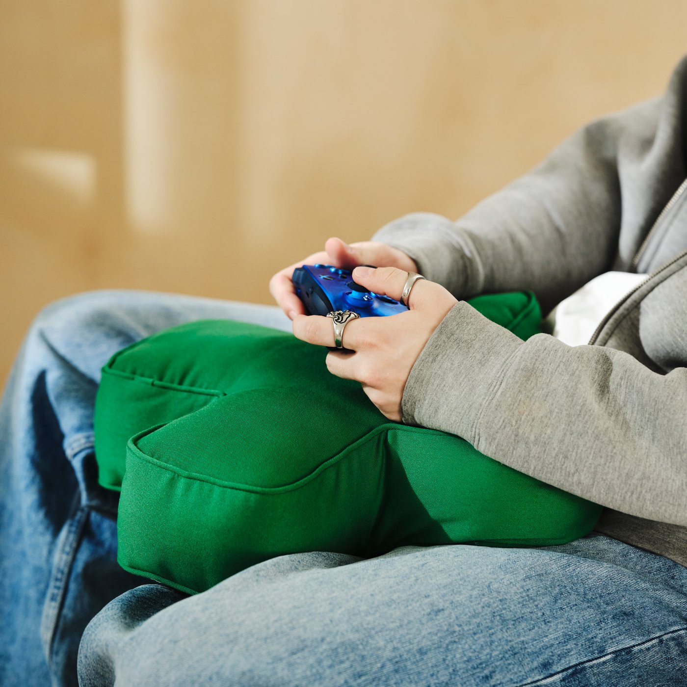 A person holding an Xbox controller while resting hands on a green D-pad-inspired cushion.