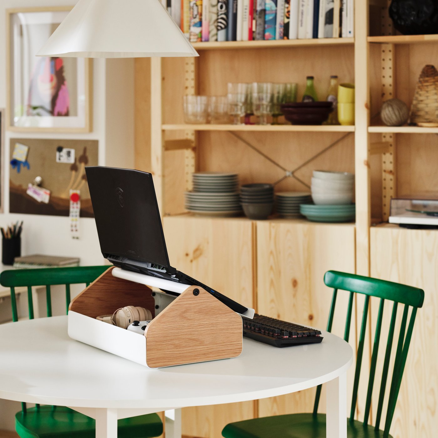 A gaming storage stand supporting a laptop with accessories stored underneath on a dining table.